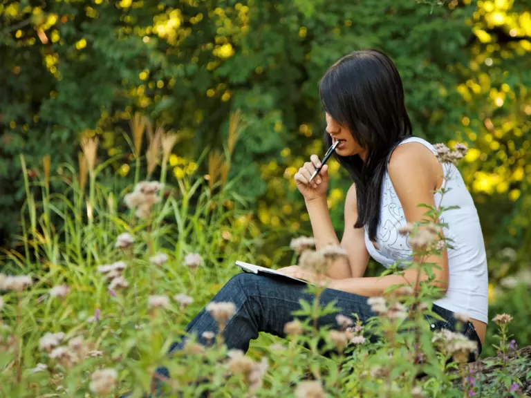 Woman writing in her journal while sitting in a garden.